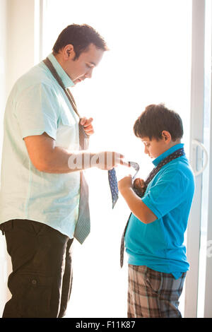 Hispanic father showing son how to tie necktie Stock Photo