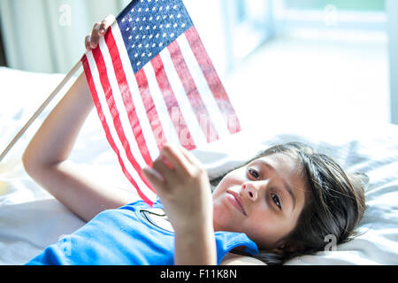 Hispanic girl holding American flag on bed Stock Photo