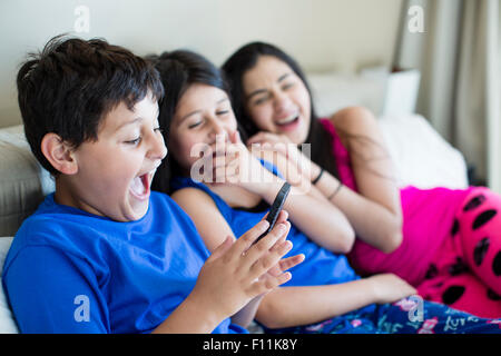 Hispanic siblings using cell phone on sofa Stock Photo
