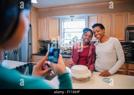 Black woman photographing sister and mother in kitchen Stock Photo
