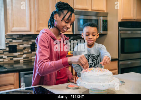 Black brother and sister decorating cake in kitchen Stock Photo