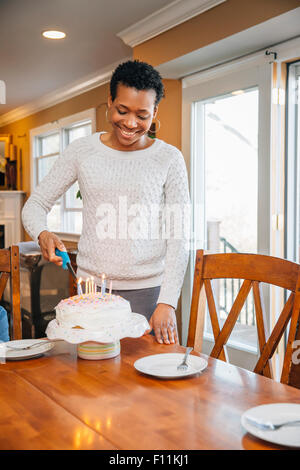Black woman lighting candles on birthday cake Stock Photo