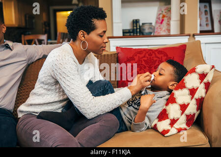 Black woman wiping nose of son on sofa Stock Photo