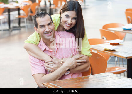 Hispanic couple hugging at sidewalk cafe Stock Photo