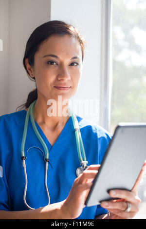 Mixed race nurse using digital tablet at window Stock Photo