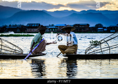 Asian fishermen sharing tea in canoes on river Stock Photo