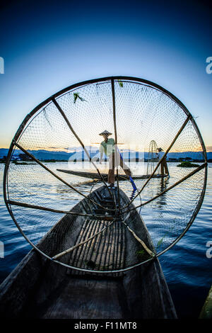 Asian fisherman using fishing net in canoe on river Stock Photo