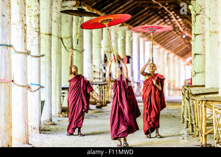 Asian monks-in-training playing with parasols in hallway Stock Photo