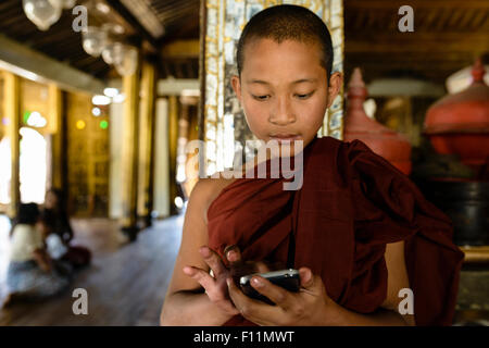 Asian monk-in-training using cell phone indoors Stock Photo