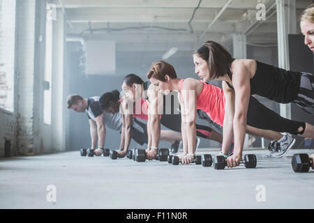 Athletes doing push-ups with dumbbells on floor Stock Photo