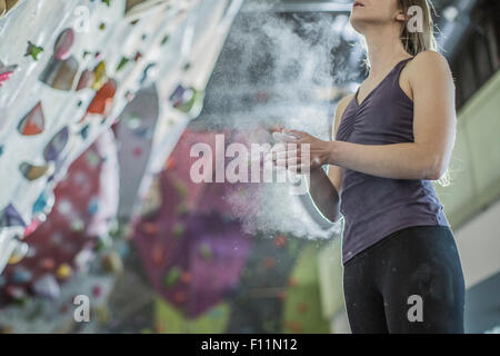 Athlete chalking her hands at rock wall in gym Stock Photo