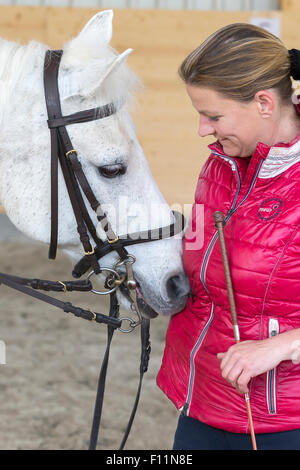 German Riding Pony Rider after riding lesson smoothing white pony Stock Photo