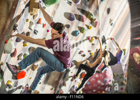 Athletes climbing rock wall in gym Stock Photo