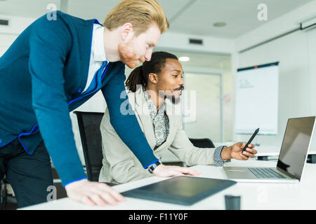 A black young man with dreadlocks and a young handsome red haired businessman discussing graphics design flaws in a nice white o Stock Photo