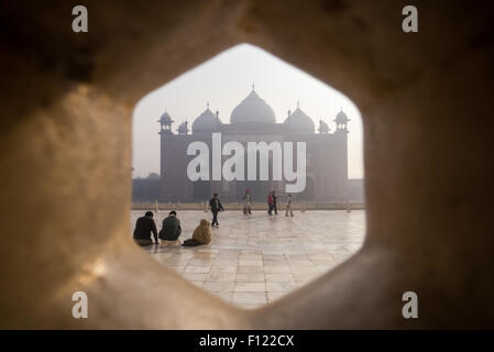 Agra, Uttar Pradesh, India. The Taj Mahal; main mausoleum; tourists and the Jawab building with its three domes outside seen through a lattice screen. Stock Photo