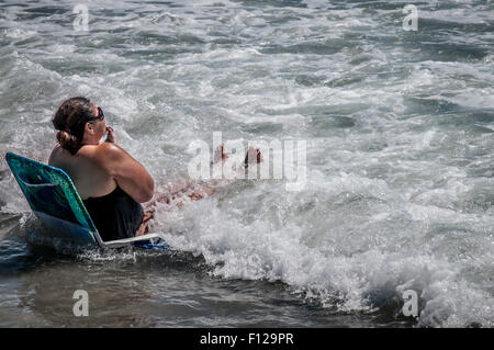 A WET SURPRISE,This woman  sitting in her folding chair at the ocean edge,got a wet surprise as the high tide started to come in Stock Photo