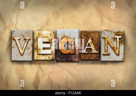 The word 'VEGAN' written in rusty metal letterpress type on a crumbled aged paper background. Stock Photo