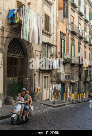 Family on motorcycle passes under woman on balcony tending drying laundry in Naples Italy Stock Photo