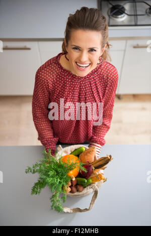 Delighted after a trip to the local market, a woman is smiling and laughing, looking up from her bag of fresh produce which includes a wide variety of fall vegetables. Stock Photo