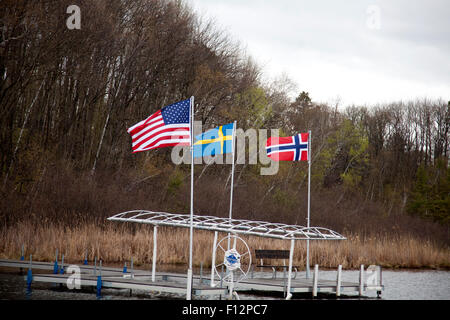 Flags of United States, Sweden and Norway flying on a boat dock over water near Roy Lake. Nisswa Minnesota MN USA Stock Photo