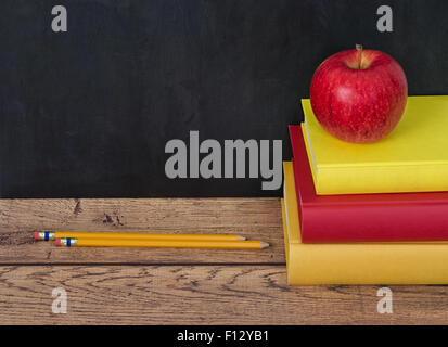 Stack of school books with apple and pencils on the desk. Chalkboard in the background with copy space. Stock Photo