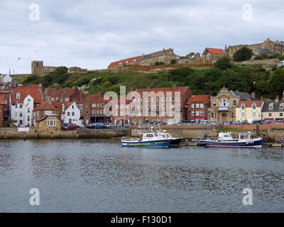 Fishing boats moored up in the harbor with houses and a church on the hill in the background Stock Photo