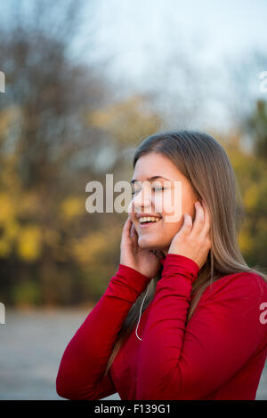 Young happy woman listening  music with headphones and singing in autumn park, wearing red pullover Stock Photo