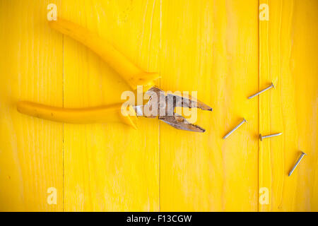 Pliers and few nails on the yellow wood surface Stock Photo