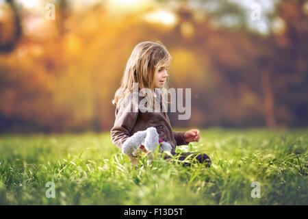 Girl sitting in a field holding a soft toy Stock Photo