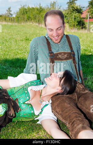 couple in traditional bavarian clothes sitting in the grass Stock Photo