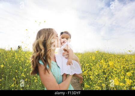 Mother kissing baby girl in field of flowers