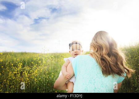 Rear view of woman walking in field and holding her baby girl Stock Photo