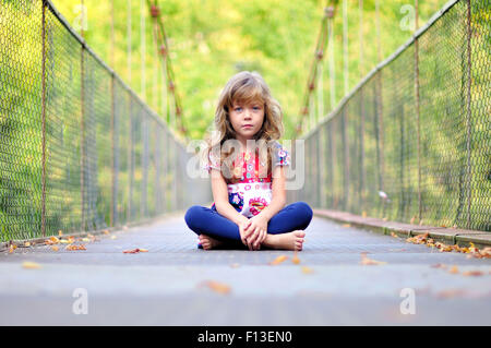 Portrait of a little girl sitting on a bridge Stock Photo