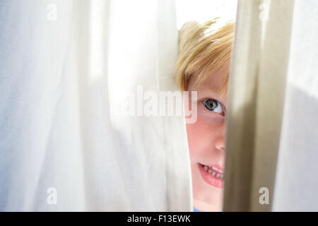 Boy looking out from behind a curtain Stock Photo