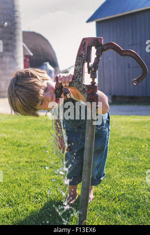 Boy drinking water from an outdoor tap on a farm Stock Photo