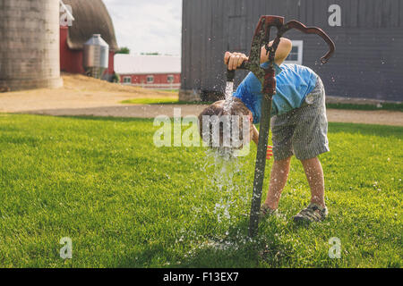 Boy putting his head under a water tap on a farm Stock Photo