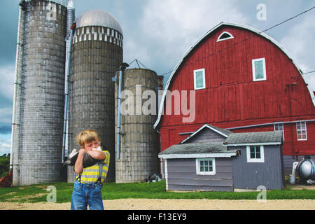 Boy standing on a farm cuddling a cat, USA Stock Photo