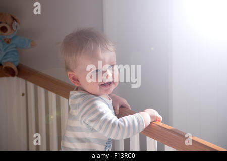 Baby boy in nursery waking up in his white cot with teddy in the background. Stock Photo