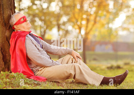 Senior in superhero outfit leaning on tree in park Stock Photo