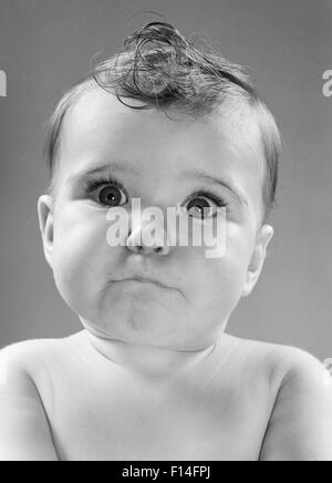 1950s BABY MAKING FUNNY FACE WITH WIDE OPEN EYES THIN MOUTH PURSED LIPS LOOKING AT CAMERA Stock Photo