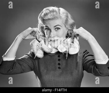 1950s PORTRAIT BLOND WOMAN HOLDING UP A PAIR OF BABY BOOTIES IN EACH HAND LOOKING AT CAMERA Stock Photo