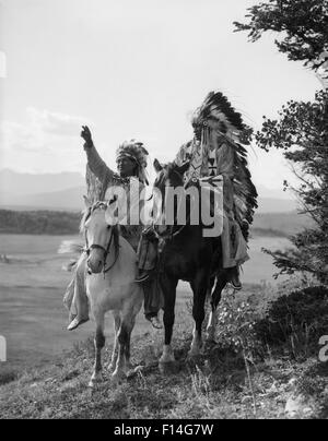 1920s TWO NATIVE AMERICAN INDIAN MEN ON HORSEBACK IN FULL FEATHER HEADDRESS STONEY SIOUX TRIBE ALBERTA CANADA Stock Photo