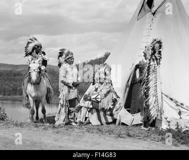 1920s FOUR NATIVE AMERICAN STONEY SIOUX INDIAN MEN ASSEMBLED BESIDE TEPEE WEARING FULL EAGLE FEATHER WAR BONNETS ALBERTA CANADA Stock Photo