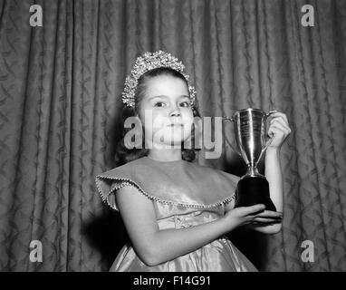 1950s 1960s YOUNG GIRL STANDING WITH TROPHY LOVING CUP WEARING TIARA PRETTY DRESS WINNER OF BEAUTY PAGEANT LOOKING AT CAMERA Stock Photo