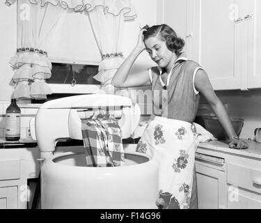 1950s FRUSTRATED HOUSEWIFE WITH JAMMED WRINGER ON CLOTHES WASHING MACHINE IN KITCHEN Stock Photo