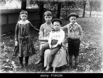 1890s 1900s FAMILY GROUP PORTRAIT SIBLINGS GIRL SISTER TWO BOYS BROTHERS OUTSIDE IN BACKYARD WITH MOTHER LOOKING AT CAMERA Stock Photo