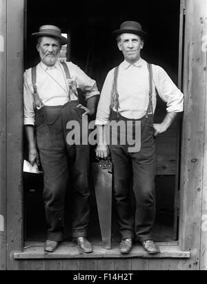 1890s 1895 PORTRAIT OF TWO WORKMEN STANDING IN OPEN DOORWAY HOLDING CARPENTER TOOLS LOOKING AT CAMERA Stock Photo