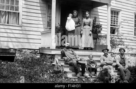 1890s GROUP PORTRAIT FAMILY ADULTS CHILDREN POSING SITTING STANDING ON FRONT PORCH OF HOUSE LOOKING AT CAMERA Stock Photo