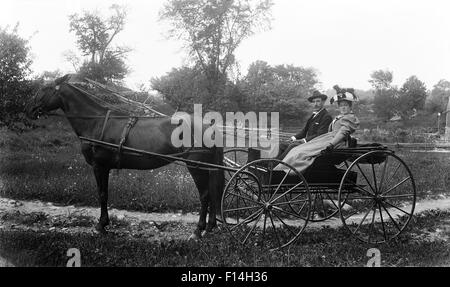 1890s TURN OF THE 20TH CENTURY COUPLE MAN WOMAN RIDING IN HORSE DRAWN BUGGY CARRIAGE LOOKING AT CAMERA Stock Photo