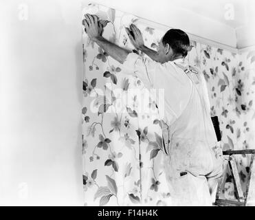 1940s MAN HANGING FLORAL PATTERN WALLPAPER Stock Photo